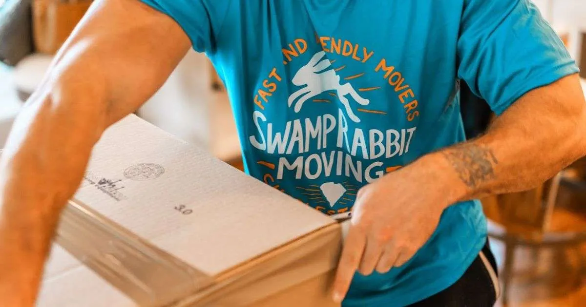 A man in a blue shirt holds a box, representing Swamp Rabbit Moving & Storage in South Carolina.