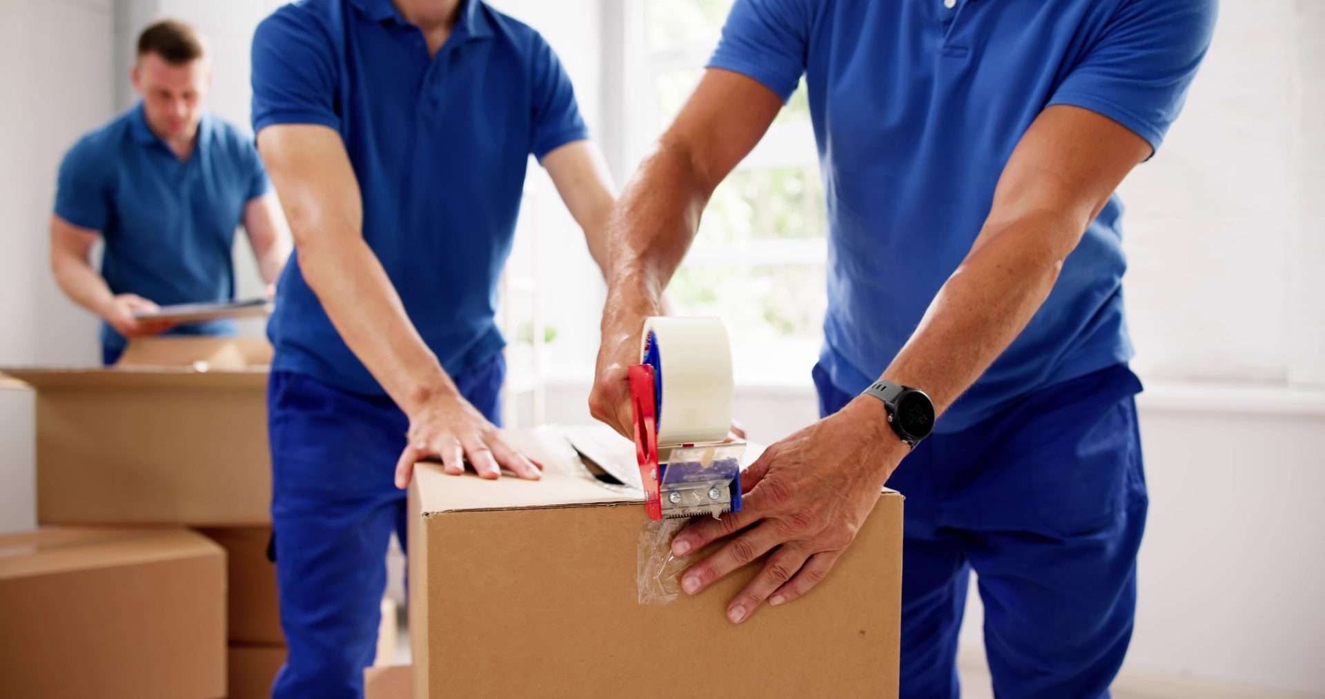 Two movers pictured from the shoulders down, taping up a box.