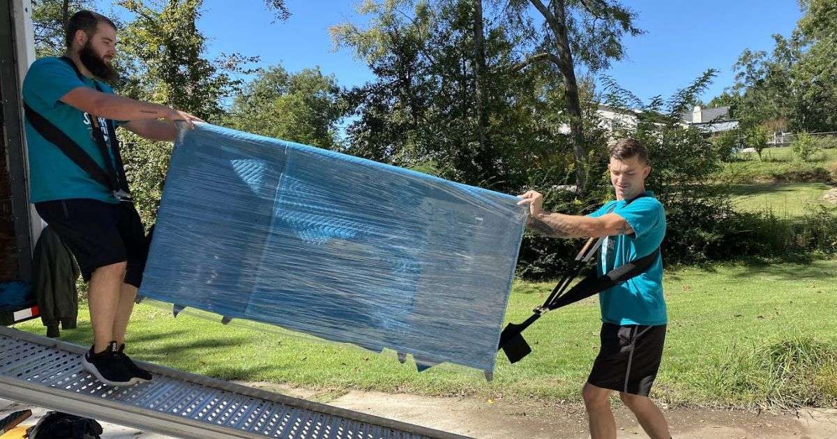Two Swamp Rabbit commercial movers in Greenville on a moving truck ramp carefully load heavy, wrapped furniture using furniture straps