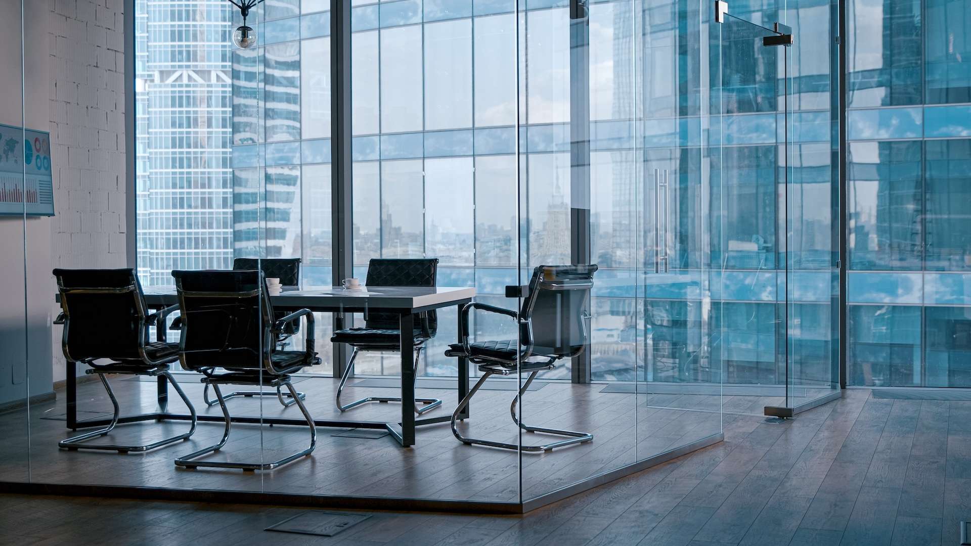 Empty meeting room with glass walls, a desk, and five black office chairs.