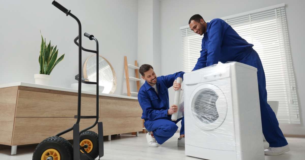 Two Greenville intrastate movers wrapping and moving an appliance.