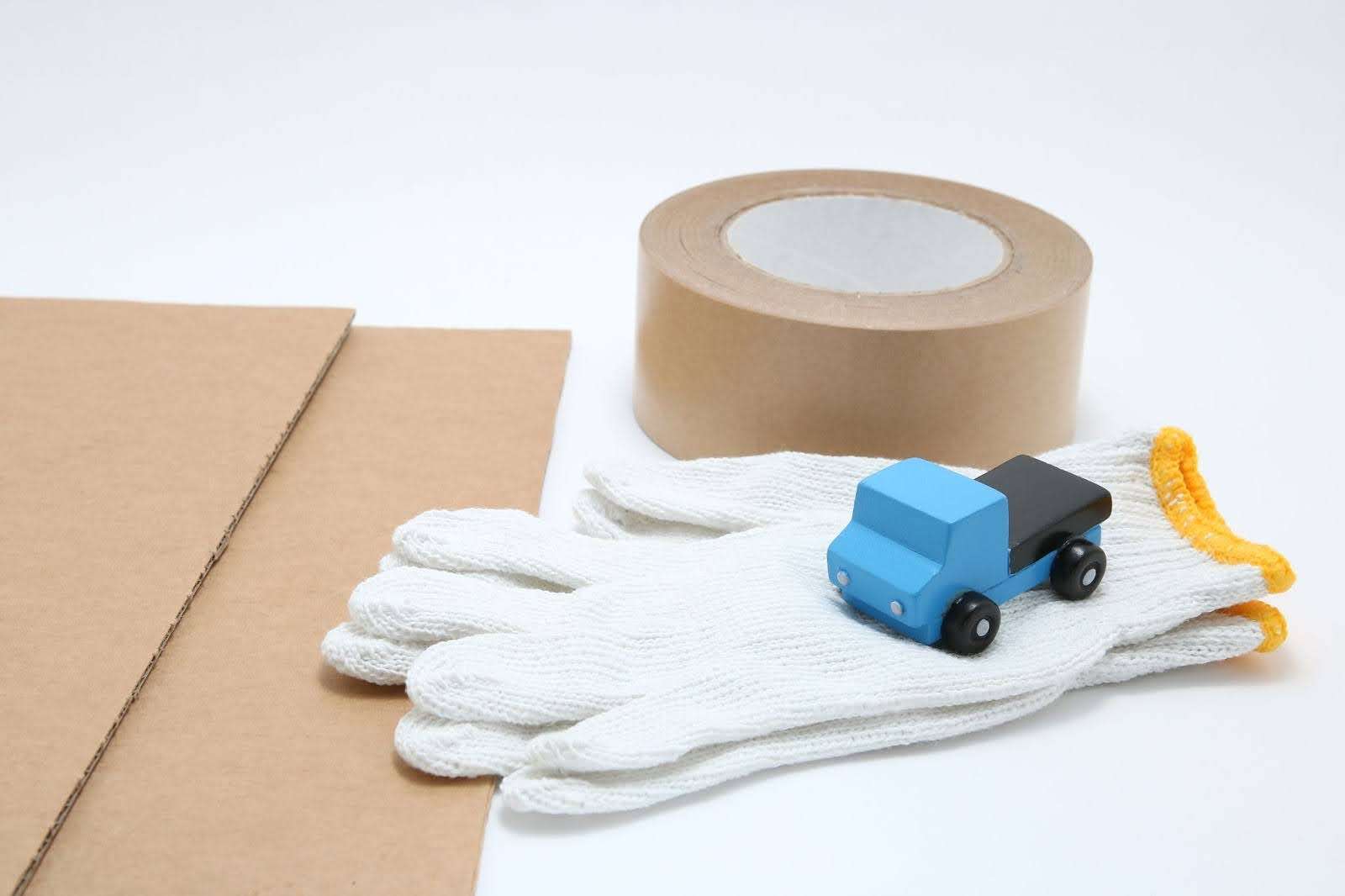 Toy mini car truck, packing tape, card boards, and cotton work gloves on white background.